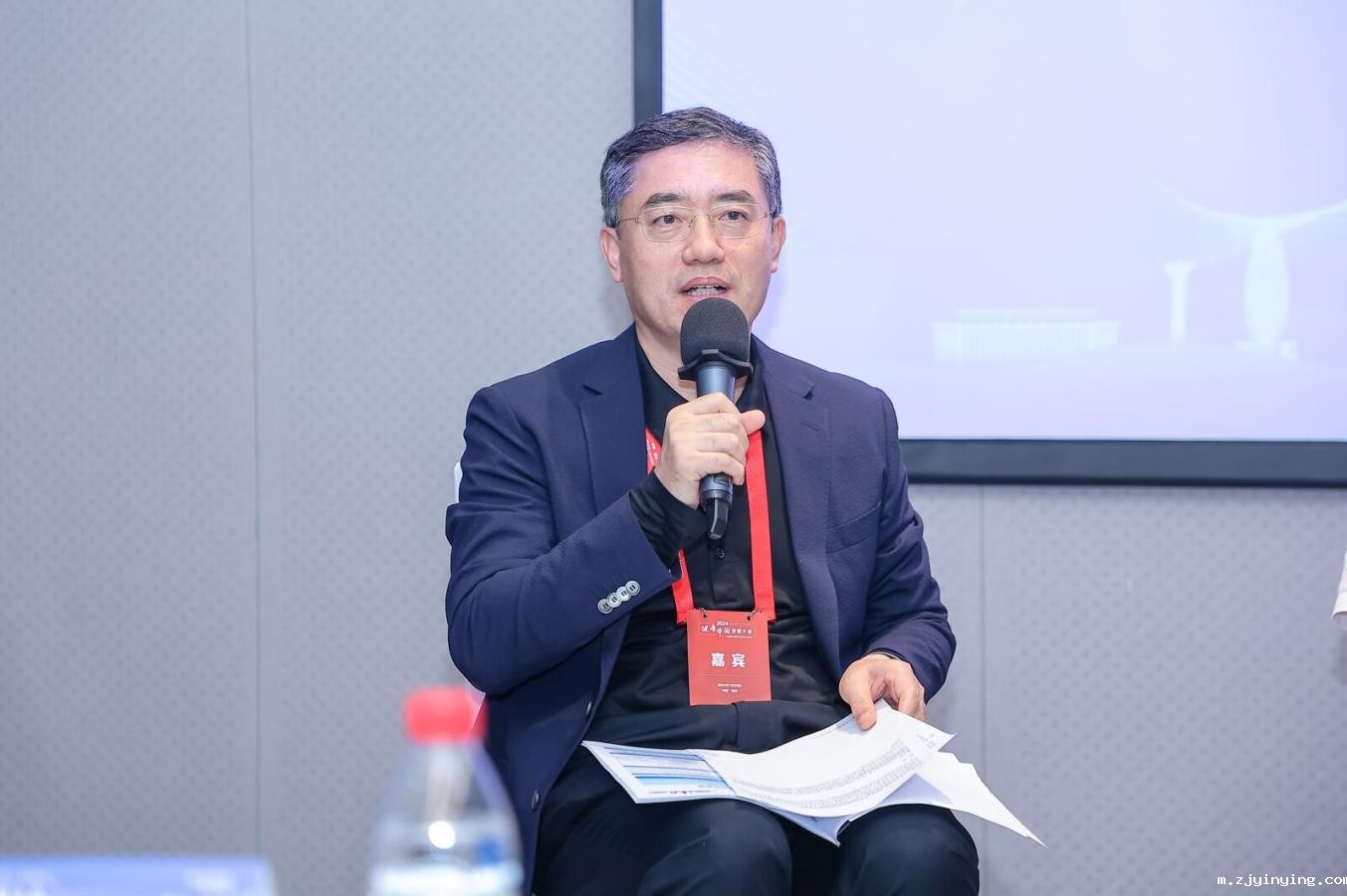 A person sitting in a chair holding a microphoneDescription automatically generated